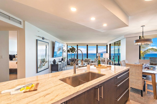 kitchen with light stone countertops, sink, hanging light fixtures, expansive windows, and dark brown cabinets