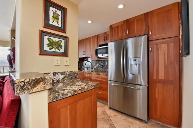 kitchen with sink, tasteful backsplash, dark stone counters, kitchen peninsula, and stainless steel appliances