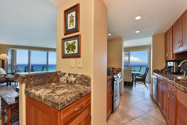 kitchen with sink, stainless steel appliances, a water view, light tile patterned flooring, and dark stone counters