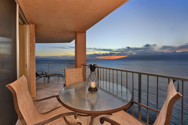 balcony at dusk featuring a water view