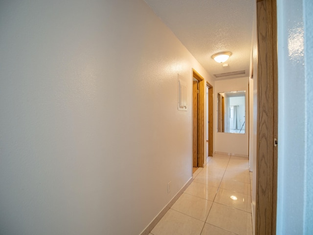 hall with a textured ceiling and light tile patterned flooring