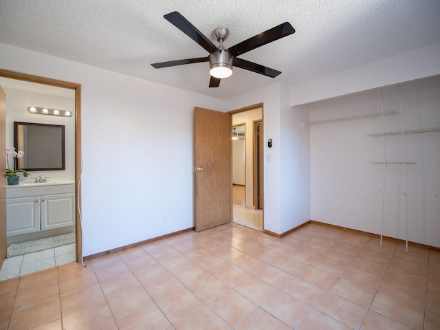 unfurnished bedroom featuring sink, a textured ceiling, ceiling fan, light tile patterned floors, and ensuite bath