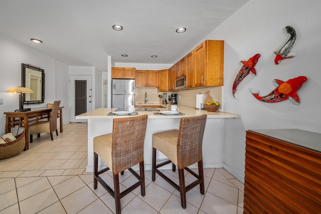 kitchen with appliances with stainless steel finishes, light tile patterned floors, kitchen peninsula, and sink