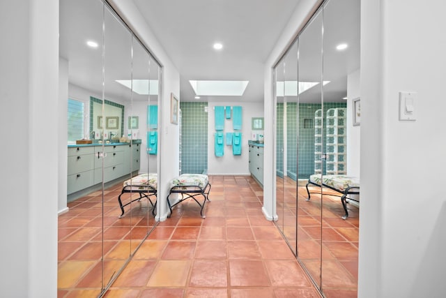 corridor with light tile flooring, a skylight, and sink