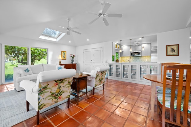 tiled living room with lofted ceiling with skylight and ceiling fan