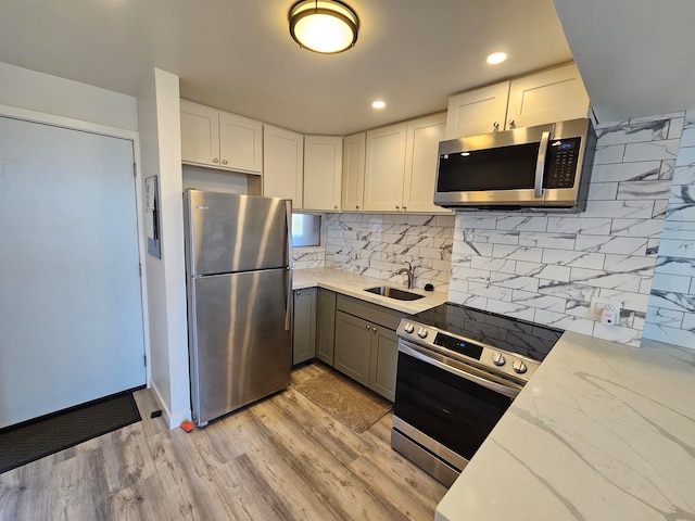 kitchen featuring white cabinetry, light wood-type flooring, appliances with stainless steel finishes, light stone countertops, and sink