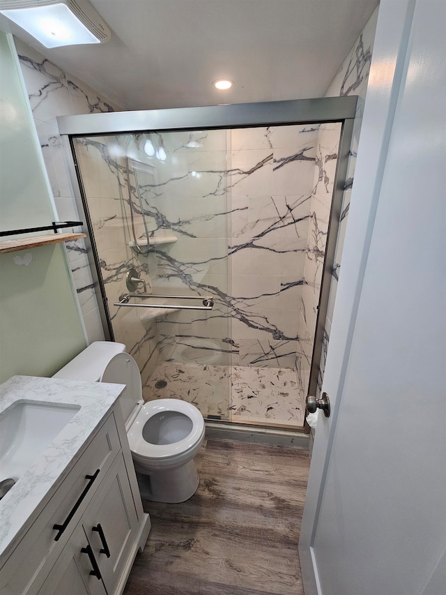 bathroom featuring hardwood / wood-style flooring, a shower with shower door, vanity, and toilet