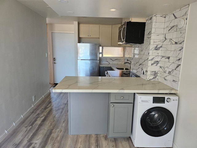 kitchen featuring wood-type flooring, kitchen peninsula, decorative backsplash, appliances with stainless steel finishes, and washer / dryer