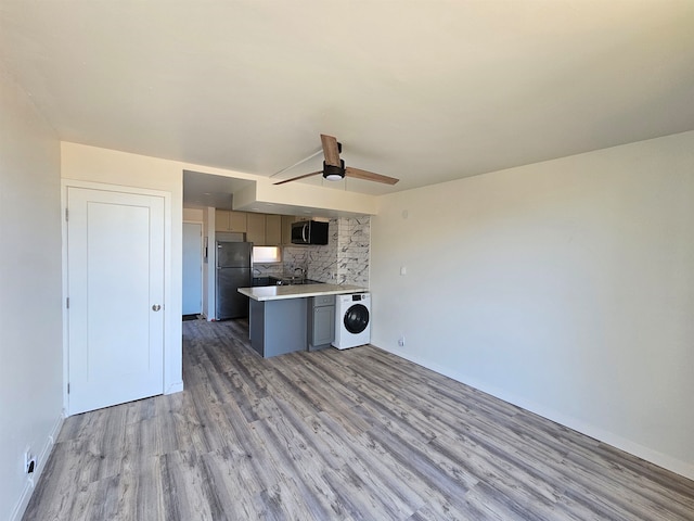 kitchen featuring kitchen peninsula, tasteful backsplash, light wood-type flooring, appliances with stainless steel finishes, and washer / dryer