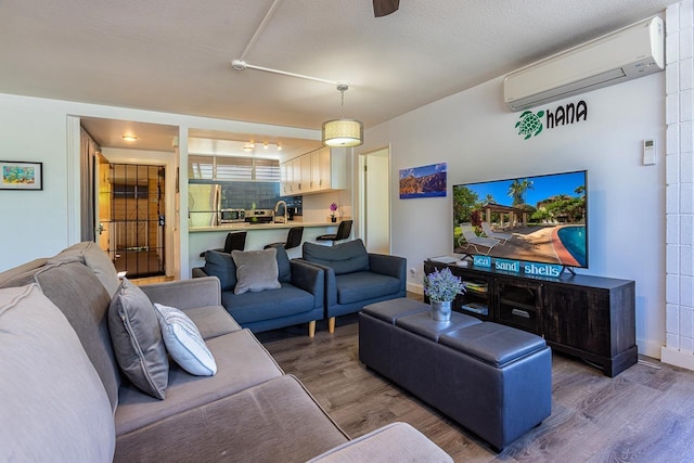 living room with a wall mounted air conditioner, dark hardwood / wood-style flooring, sink, and a textured ceiling