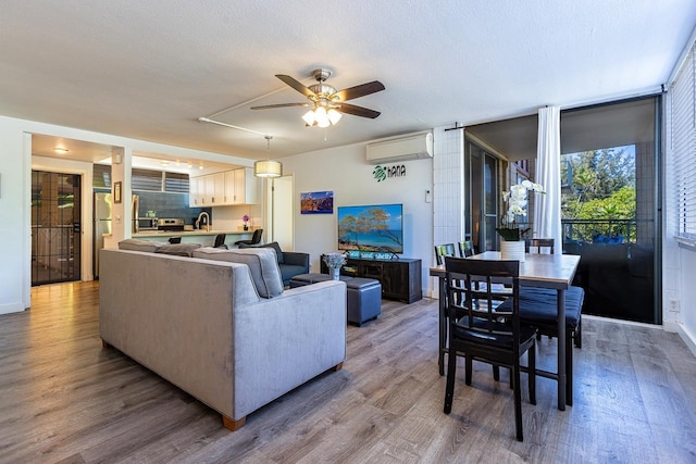 living room with a textured ceiling, ceiling fan, wood-type flooring, and a wall mounted air conditioner