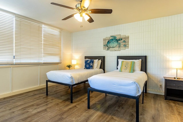 bedroom featuring wood-type flooring, ceiling fan, and tile walls