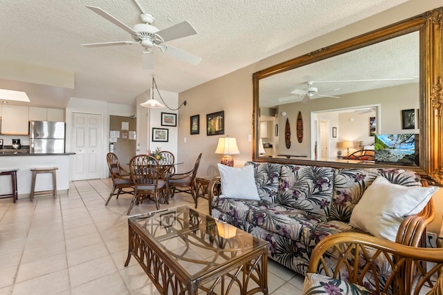 living area with a ceiling fan, light tile patterned floors, and a textured ceiling