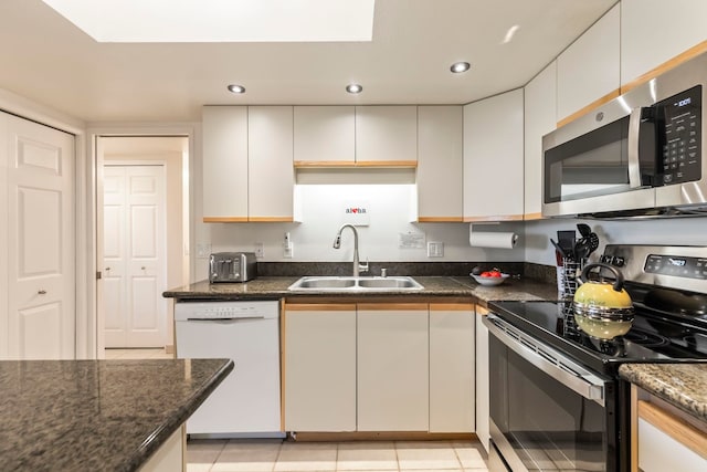 kitchen with a sink, stainless steel appliances, dark stone countertops, light tile patterned flooring, and recessed lighting
