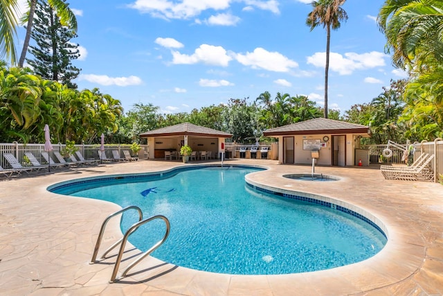pool with an outbuilding, a patio, a community hot tub, and fence