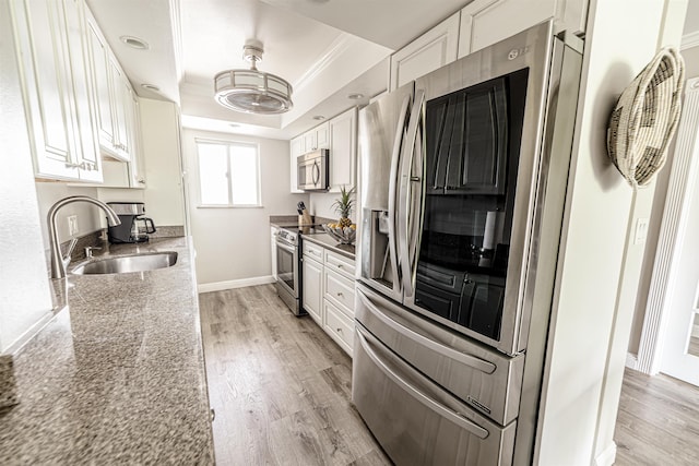 kitchen with a tray ceiling, a sink, light wood-type flooring, and appliances with stainless steel finishes