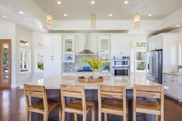 kitchen with white cabinets, glass insert cabinets, appliances with stainless steel finishes, wall chimney range hood, and tasteful backsplash