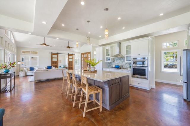 kitchen featuring tasteful backsplash, finished concrete floors, a barn door, stainless steel appliances, and wall chimney exhaust hood