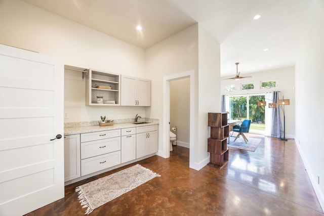 kitchen with a sink, concrete floors, baseboards, light stone counters, and open shelves