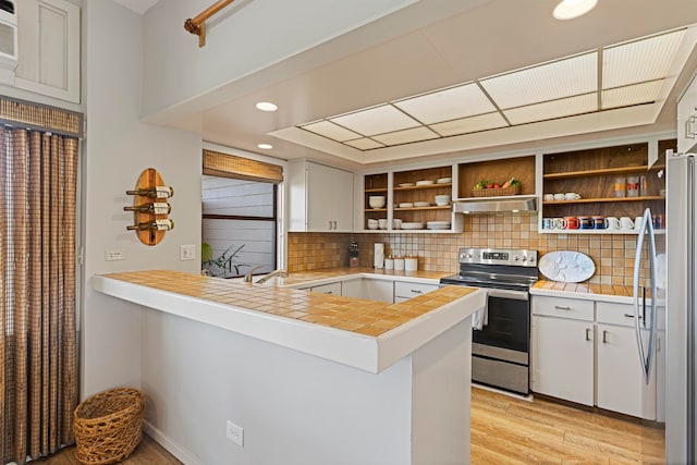 kitchen with white cabinetry, backsplash, kitchen peninsula, stainless steel appliances, and light wood-type flooring