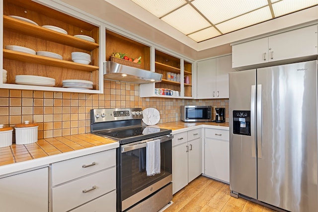 kitchen with exhaust hood, stainless steel appliances, tile countertops, and white cabinets