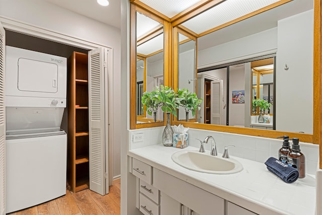 bathroom featuring wood-type flooring, vanity, stacked washer / drying machine, and tasteful backsplash