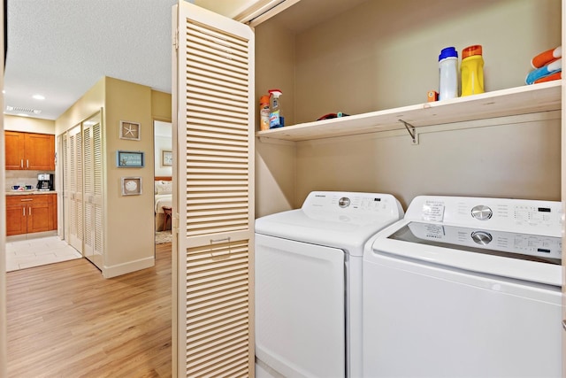 laundry room featuring independent washer and dryer, light wood-type flooring, and a textured ceiling