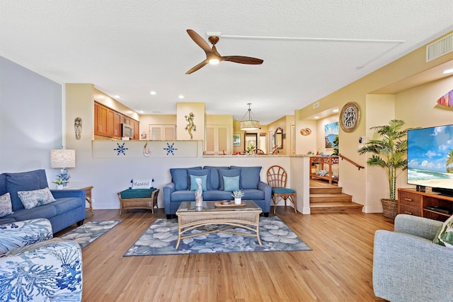 living room featuring ceiling fan, light hardwood / wood-style floors, and a textured ceiling