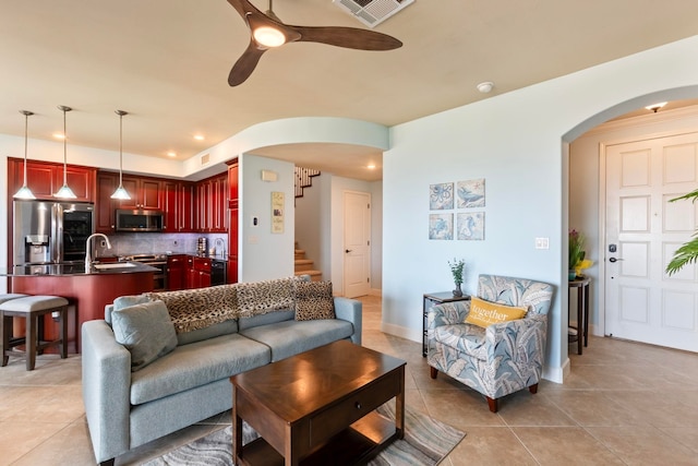 living room featuring visible vents, stairs, a ceiling fan, arched walkways, and light tile patterned floors