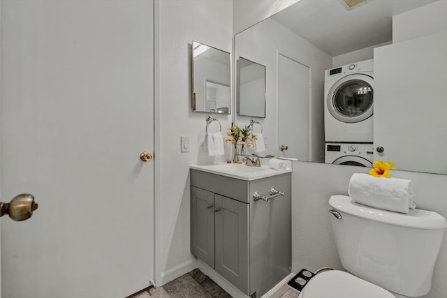 bathroom featuring stacked washer / dryer, vanity, and toilet