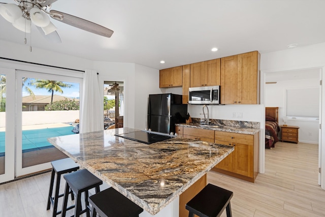 kitchen with ceiling fan, a breakfast bar area, light hardwood / wood-style flooring, black appliances, and stone counters