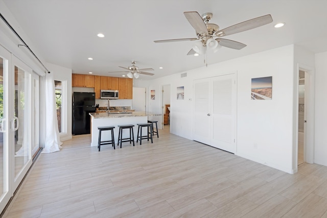 kitchen with a kitchen breakfast bar, black refrigerator, light stone countertops, a center island, and light wood-type flooring