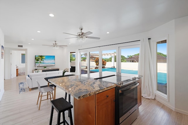 kitchen with a kitchen island, a kitchen breakfast bar, light stone countertops, light hardwood / wood-style flooring, and stainless steel range with electric stovetop