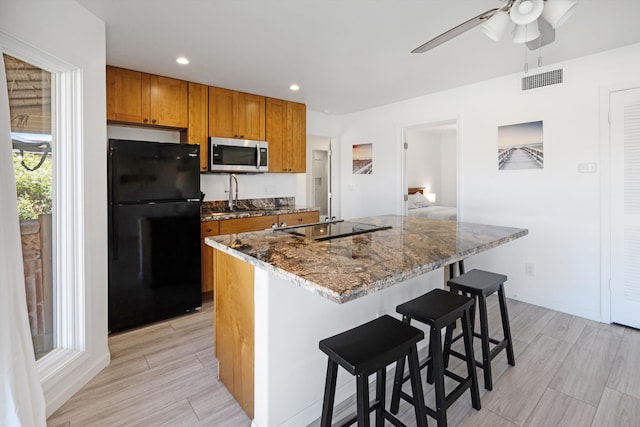 kitchen featuring a breakfast bar, black appliances, and a center island with sink