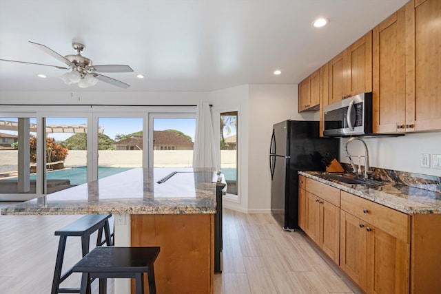 kitchen featuring stone countertops, sink, a breakfast bar, light hardwood / wood-style floors, and ceiling fan