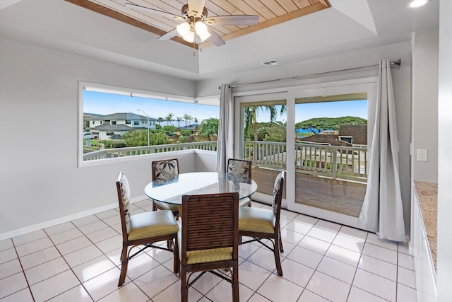 tiled dining area with ceiling fan and a raised ceiling