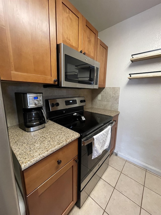 kitchen with stainless steel appliances, tasteful backsplash, light tile patterned floors, and light stone counters