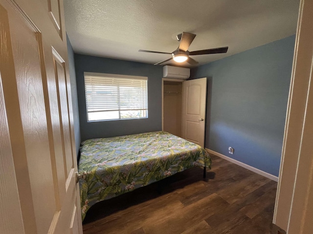 bedroom featuring a wall mounted air conditioner, ceiling fan, multiple closets, dark wood-type flooring, and a textured ceiling