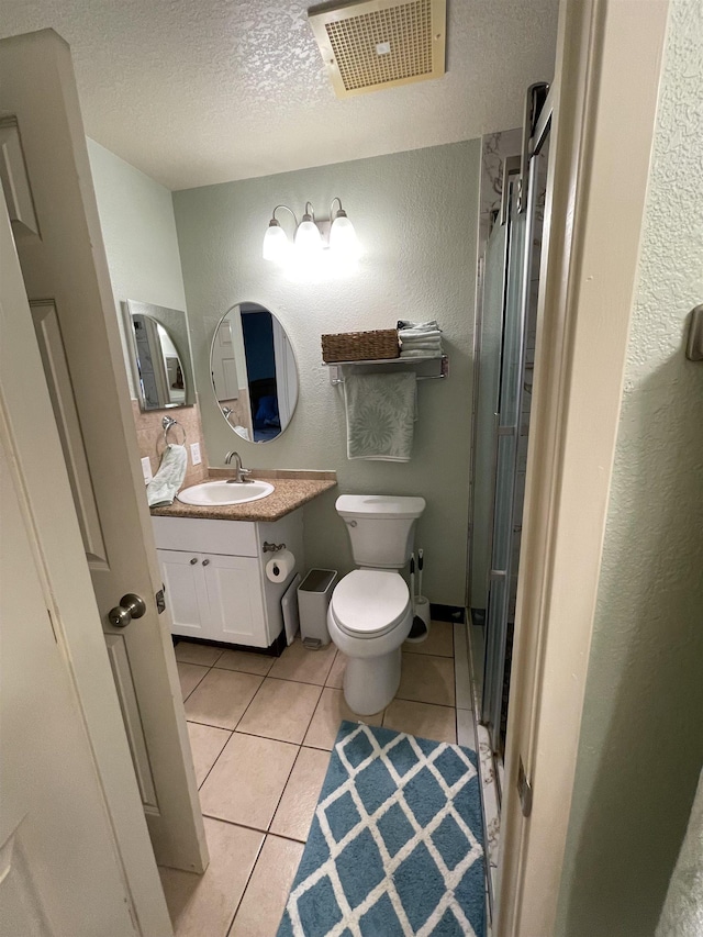 bathroom featuring tile patterned flooring, vanity, a textured ceiling, toilet, and walk in shower