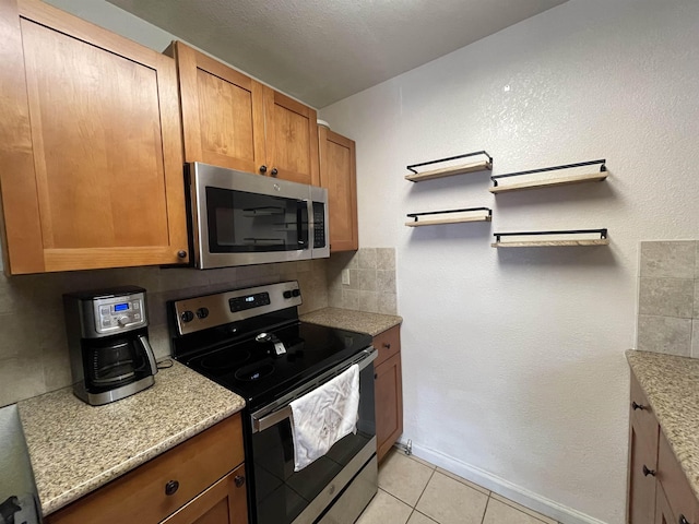 kitchen with light stone counters, appliances with stainless steel finishes, light tile patterned floors, and backsplash