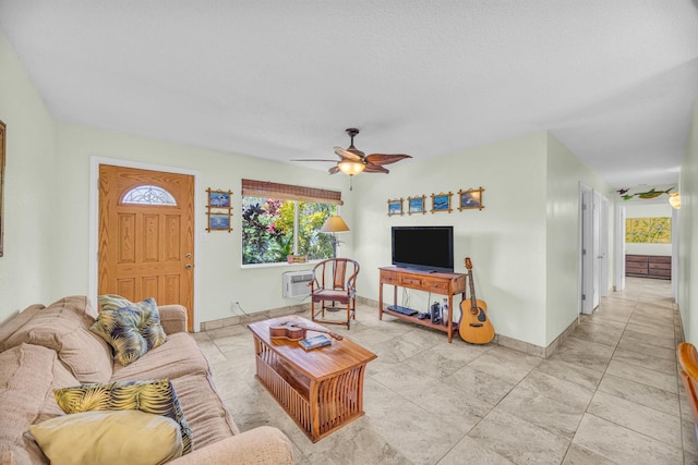 living room with baseboards, a wall unit AC, and a ceiling fan