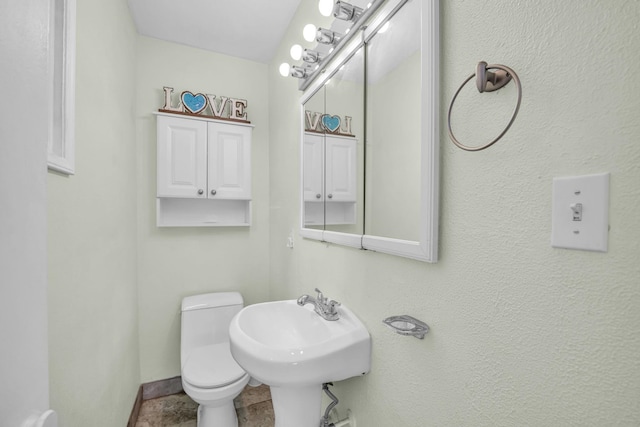half bathroom featuring baseboards, toilet, and a sink