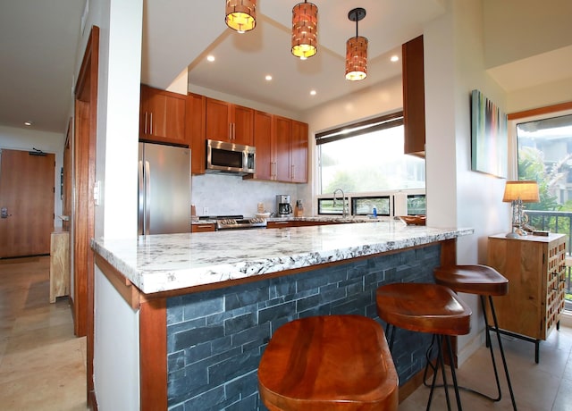 kitchen featuring light tile flooring, kitchen peninsula, appliances with stainless steel finishes, hanging light fixtures, and light stone counters