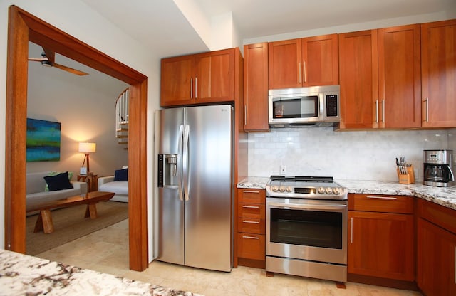 kitchen featuring stainless steel appliances, ceiling fan, light tile floors, and light stone countertops