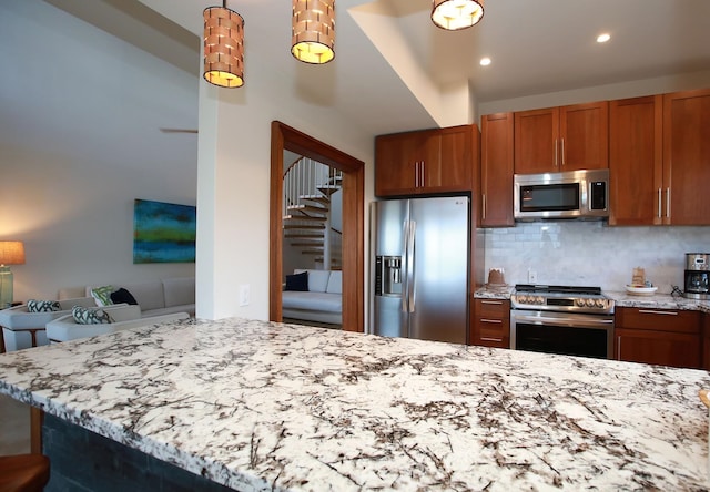 kitchen with backsplash, light stone countertops, stainless steel appliances, and decorative light fixtures