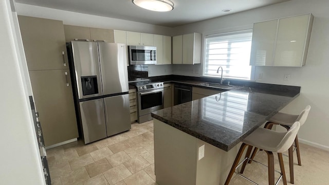 kitchen with dark stone counters, a kitchen breakfast bar, a peninsula, stainless steel appliances, and a sink