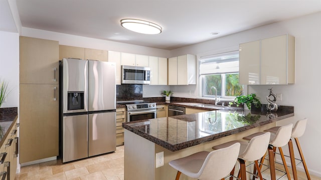 kitchen featuring a breakfast bar, dark stone countertops, a peninsula, stainless steel appliances, and a sink