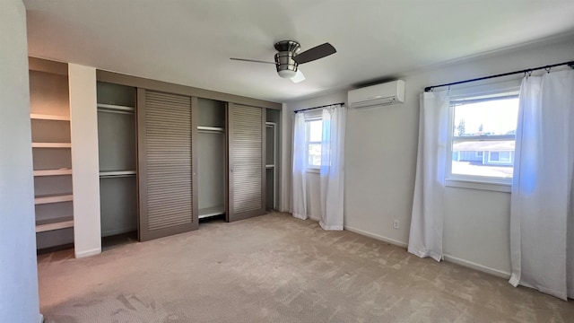 unfurnished bedroom featuring ceiling fan, light carpet, multiple closets, and a wall mounted air conditioner