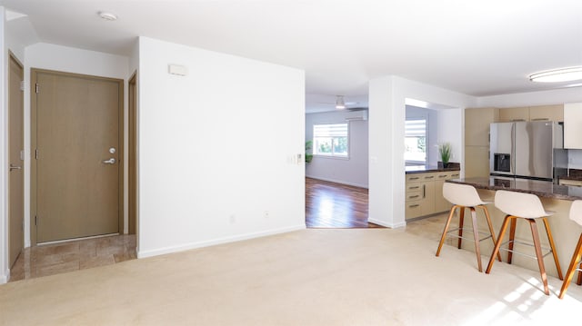 kitchen featuring light carpet, stainless steel refrigerator with ice dispenser, a breakfast bar, and baseboards