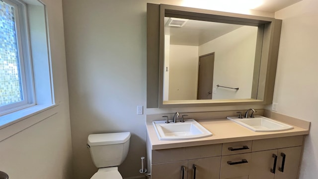 bathroom with visible vents, double vanity, a sink, and toilet